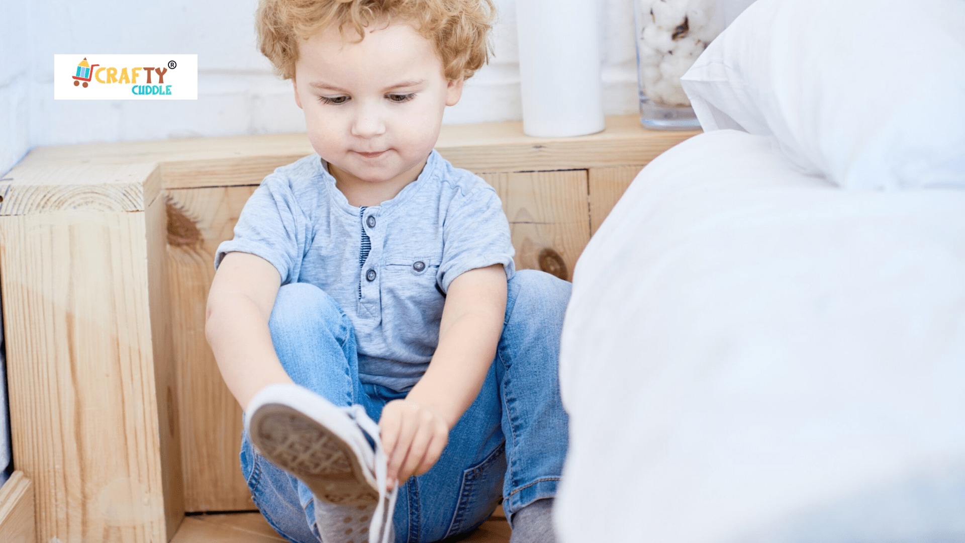 A small children trying to wear shoes in the left hand while sitting on the sofa.