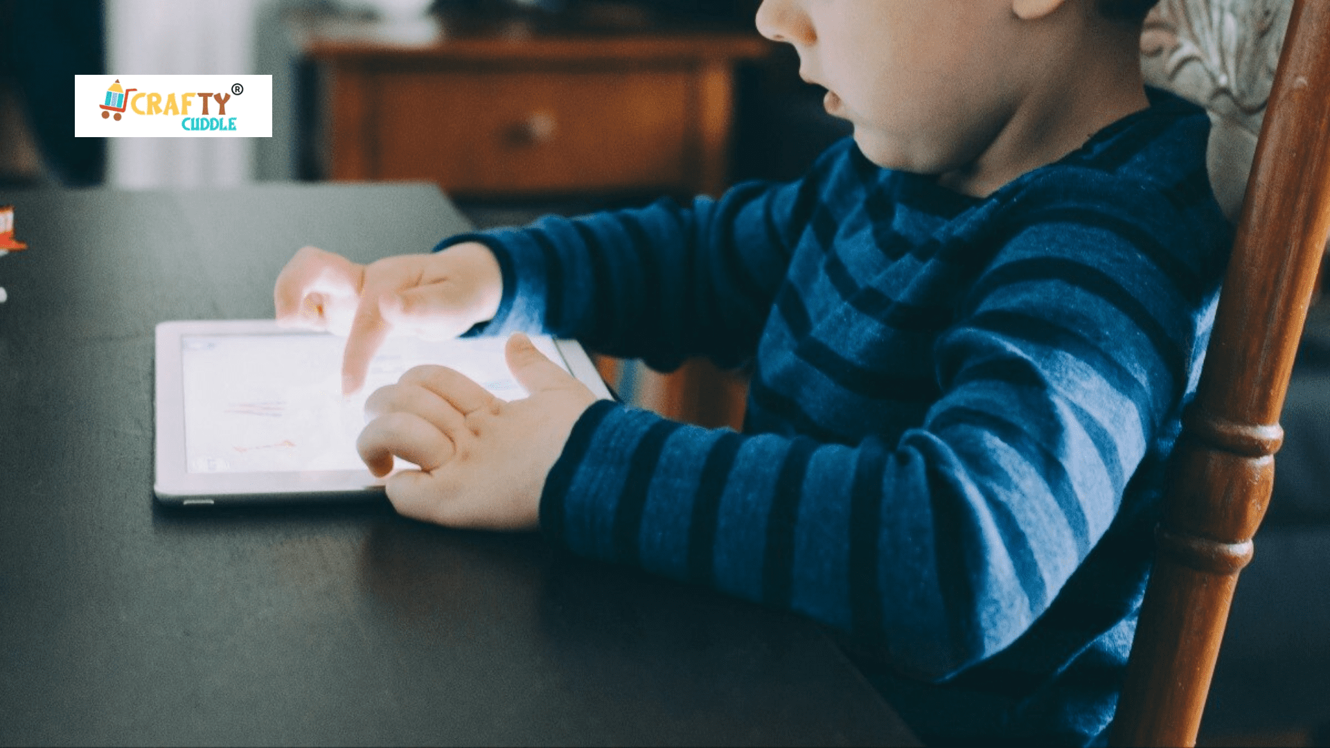 A small children plays video game in the tablet while siting on the table.