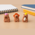 Capybara ErasersErasersCRAFTY CUDDLEThree animal - themed erasers on a wooden surface with notebooks and pencils in the background.1AnimalLoversCapybaraArt