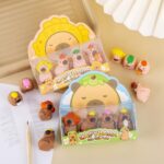 Capybara-shaped erasers in packaging on a light surface with a pencil and notebook.