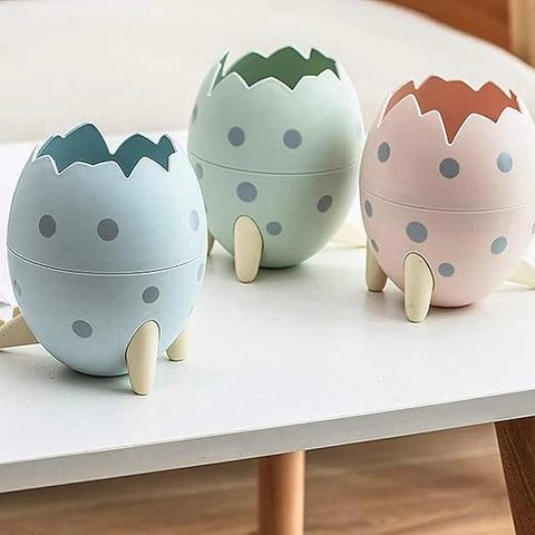 image includes 3 Dino egg pen stand in different colors placed on a table.