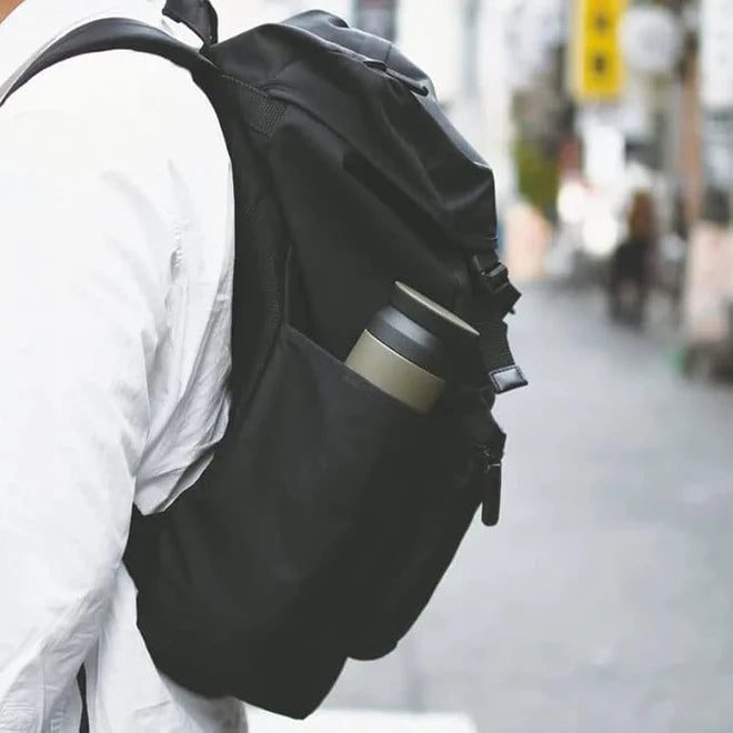 A image of man holding black color bag pack with stainless steel bottle in its side pocket.