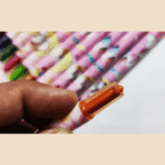 Close-up of a hand holding an orange pen with a colorful pencil background