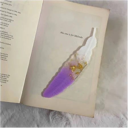 A image of purple and white colored feather placed on the one page of the opened book.
