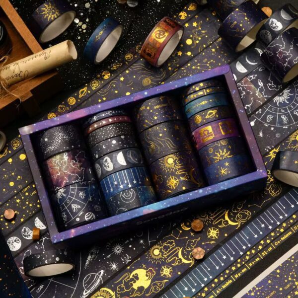 Set of washi tape rolls with celestial designs in a decorative box on a matching background.