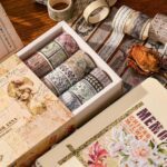 Collection of decorative washi tape rolls in a box on a wooden surface.