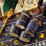 Washi Tape – 20 pcs Vast Universe SeriesCRAFTY CUDDLEWashi Tapes with celestial designs on a starry night - themed surface with a quill and book.