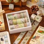 Washi Tape Box of 20 – Wilderness RemainsCRAFTY CUDDLESet of decorative washi tape rolls in a box on a wooden surface with additional rolls scattered around.
