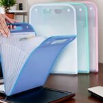 Transparent blue file holder with a stack of papers on a desk, with other holders in the background.