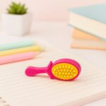 Pink and yellow brush on a notebook page with stationery items in the background