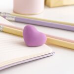 Purple heart-shaped eraser on a notebook with pencils in the background