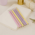 Pastel-colored pencils on a notebook with a gold cup and gift box in the background.