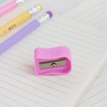 Pink pencil sharpener on a lined notebook with colorful pens in the background