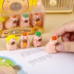 Cute pink capybara figurines with accessories on a desk, with packaging in the background.
