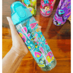 Colorful water bottle with butterfly design held by a hand on a wooden surface