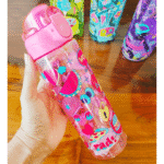 Colorful water bottle with cartoon designs held by a hand on a wooden surface