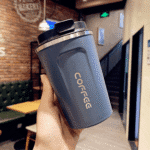 Blue coffee tumbler with 'COFFEE' text held in a hand inside a cafe.