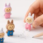 Labubu ErasersErasersCRAFTY CUDDLEThree cartoon character erasers in pink, blue, and white outfits on a notebook with a pencil.1CharacterErasersCuteErasers