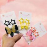 Handmade hair clips on cards held by a hand against a pink background