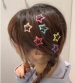 Colorful star-shaped hair clips on a person's braided hair against a neutral background