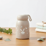 Leak Proof Rabbit Print Glass BottleCartoon Kids Water BottleCRAFTY CUDDLEBeige bottle with rabbit design on a wooden surfaceBeigeKidsGlassBottle 350mlBottle GlassWaterBottle RabbitPrintBottle LeakProofBottle SiliconeCoverBottle ToddlerWaterBottle SchoolWaterBottle BPAFreeBottle ReusableBottle