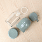 Leak Proof Rabbit Print Glass BottleCartoon Kids Water BottleCRAFTY CUDDLEClear glass jar with green silicone lid and cartoon character on a wooden surfaceSage GreenKidsGlassBottle 350mlBottle GlassWaterBottle RabbitPrintBottle LeakProofBottle SiliconeCoverBottle ToddlerWaterBottle SchoolWaterBottle BPAFreeBottle ReusableBottle