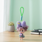 Small doll with a purple bow and green strap on a wooden surface with a light green curtain background.