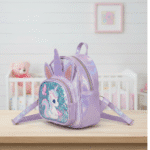 Lavender unicorn backpack on a wooden surface with a crib and teddy bear in the background