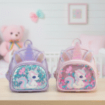 Two unicorn-themed bags on a wooden surface with a soft toy and framed picture in the background.