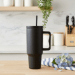 Black travel mug with handle on a wooden surface in a kitchen setting.
