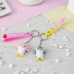 Two colorful keychains on a wooden surface with a cup and plant in the background.