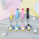 Four penguin keychains with different colored bands on a wooden surface.