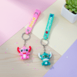 Stitch Theme Keychain with StrapKeychainsCRAFTY CUDDLETwo colorful keychains with cartoon characters on a wooden surface.1CartoonKeychain CuteKeyring MonsterKeychain KawaiiAccessories KidsBagCharm BackpackAccessory ReturnGifts TrendyKeychains SiliconeKeyring GiftForKids
