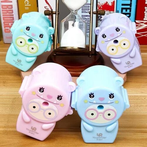 Four cute cartoon-style sharpeners on a wooden surface with books in the background.