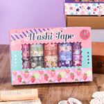 Box of Washi tape with colorful designs on a wooden surface