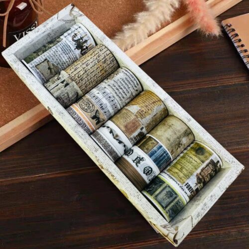 Set of washi tape rolls with vintage newspaper designs in a decorative box on a wooden surface.