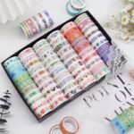 Set of colorful washi tape rolls in a box on a white surface with decorative elements.