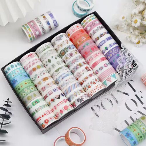 Set of colorful washi tape rolls in a box on a white surface with decorative elements.