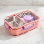 Pink lunch box with compartments and a purple lid on a light wooden surface