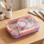 Stainless Steel Bento Lunch BoxStainless Steel Lunch BoxCrafty CuddlePink and purple bento box on a wooden table with utensils in the backgroundPinklunchbox bentobox kidslunchbox schoollunch bentolunchbox lunchboxideas leakprooflunchbox stainlesssteellunchbox schoolessentials kitchenessentials