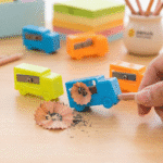 Tiny Truck SharpenerCrafty CuddleColorful pencil sharpeners on a wooden surface with a hand using one of them.1