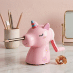 Unicorn Manual Pencil SharpenerCrafty CuddlePink unicorn - shaped pencil sharpener with a pencil inserted, on a light wooden surface with a pink background.Unicorn Sharpener PinkPink