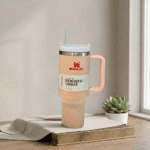 Stanley TumblerDrinkwareCrafty CuddleStanley tumbler with pink handle on a wooden surface with a plant in the backgroundStanley Tumbler-4PeachAestheticVibesAmazonFinds
