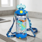 Children's water bottle with dinosaur design and blue strap on a kitchen counter