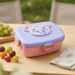 Cartoon Stainless Steel Lunch BoxStainless Steel Lunch BoxCrafty CuddlePink and purple lunch box with cartoon design on a wooden table with fruits and a napkin.Purplekidslunchbox schoollunchbox cartoonlunchbox kidslunch schoolessentials bentolunchbox kidsproducts lunchboxforkids backtoschool tiffinbox