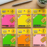Collection of colorful stick note packages on a wooden surface with a pen and plant in the background.