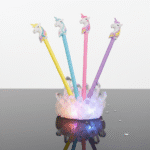 Four colorful pens with unicorn tips in a holder on a reflective surface.