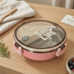 Round Stainless Steel Compartment Lunch BoxStainless Steel Lunch BoxCrafty CuddlePink lunch box with 'Smile Life' text on a wooden tablePinklunchbox bentobox tiffinbox lunchboxideas mealprep schoollunch officeessentials foodstorage kitchenessentials leakprooflunchbox