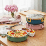 Round Stainless Steel Compartment Lunch BoxStainless Steel Lunch BoxCrafty CuddleThree Lunch box on a wooden table with food and flowers.Yellowlunchbox bentobox tiffinbox lunchboxideas mealprep schoollunch officeessentials foodstorage kitchenessentials leakprooflunchbox