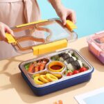 Stainless Steel Bento Lunch BoxStainless Steel Lunch BoxCrafty CuddleBento box with compartments filled with food on a light brown surface.Yellowlunchbox bentobox kidslunchbox schoollunch bentolunchbox lunchboxideas leakprooflunchbox stainlesssteellunchbox schoolessentials kitchenessentials